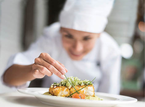 Cook decorating a plate and putting the ultimate touches - focus on foreground 