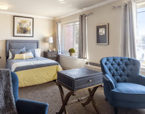 A bedroom with a bed, chair, and couch. A window with curtains. A lamp on a table. A painting on the wall. A vase with flowers. A potted plant. A car outside. AI generated content