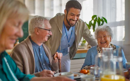 A man and woman are sitting at a table with a man standing behind them. The man standing is wearing a blue lanyard. The table is set with plates, cups, and a bowl. There are also a few oranges on the table. AI generated content